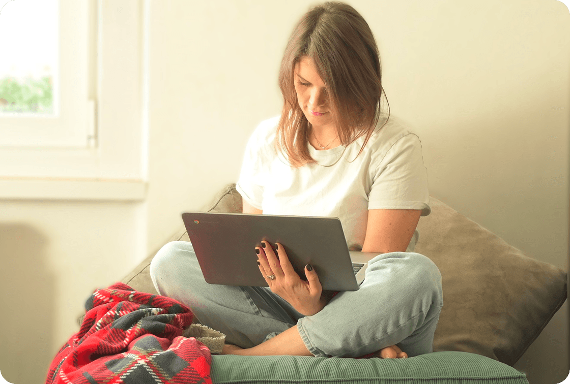 Donna seduta intenta a seguire i contenuti al pc che tiene sulle gambe incrociate